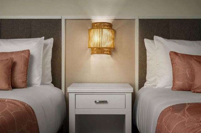 Guest room with two beds, upholstered headboards and woven wall lamp
